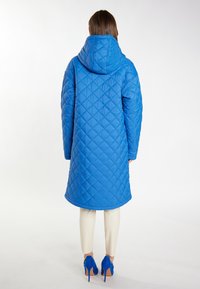 Parka căptușit albastru cu glugă, având un croi lung, larg și un model în romburi. Asortat cu pantaloni crem și pantofi cu toc înalt albaștri.