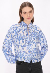 Blaue und weiße Bluse mit floralem Muster, gerüschtem Ausschnitt, langen Ärmeln und einer Knopfverschlüsse auf der Vorderseite. Leichter Stoff.