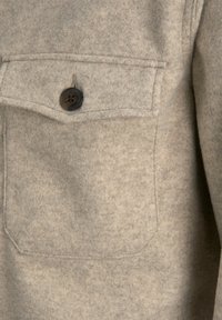 Light gray wool jacket section featuring a patch pocket and a dark button, with visible texture and stitching details.