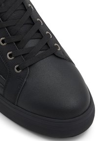 Černá sneaker s texturovaným syntetickým svrškem, kulatou špičkou, kovovými očky a plochými tkaničkami. Gumová podrážka s hladkým povrchem a minimálními akcenty.