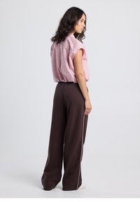 Camicia a maniche corte a righe rosa chiaro abbinata a pantaloni a gamba larga marrone scuro con piping laterale rosa. Tessuto liscio e vestibilità comoda.