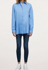 Light blue button-up shirt with a tailored fit, long sleeves, and a smooth texture, paired with dark skinny jeans and white sneakers.