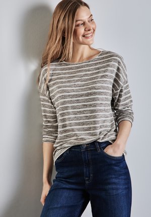 Maglietta leggera a maniche lunghe, a righe grigie e bianche, con scollatura a barca; abbinata a jeans blu scuro a gamba dritta. Tessuto liscio, vestibilità informale.