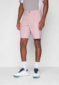 Light pink shorts with a button closure, front pockets, and subtle logo detail. Paired with white shoes and ribbed socks.