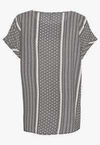 Tunic in bianco e nero con un motivo geometrico caratterizzato da design a zig zag e a diamante, maniche corte e una silhuette rilassata.
