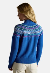 Zils adīts džemperis ar augstu apkakli un ribotām aprocēm. Izceļas ar Fair Isle rakstu baltā, zaļā un rozā krāsā visā jostā.