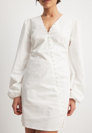 Weißes Kleid mit V-Ausschnitt, puffigen langen Ärmeln und einer Reihe dekorativer Knöpfe auf einer Seite. Aus einem glatten, leichten Stoff gefertigt.