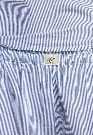 Tissu rayé vertical bleu et blanc avec une ceinture élastique froncée et une petite étiquette beige cousue avec les initiales « AJ ».