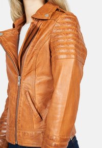 Giacca da moto in cuoio marrone con chiusura a zip, spalle texturizzate, vestibilità slim e due tasche laterali. Finitura liscia con dettagli di cucitura.