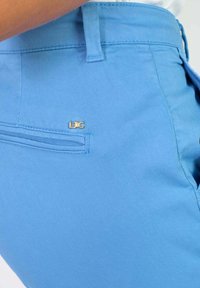 Lichtblauwe stoffen broek met een zachte textuur, voorzien van een klein gouden logo op de achterzak en een klassieke vijf-pocket stijl.