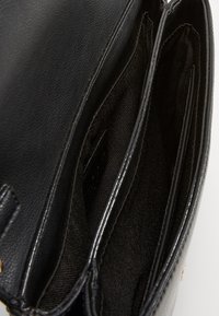 Intérieur d'un sac à main en cuir noir avec deux compartiments, texture lisse et doublure en tissu noir. Présente une petite étiquette de marque.