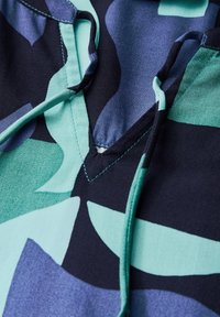 Tissu à motifs dans des nuances de bleu sarcelle et bleu marine. Col en V avec cordon de serrage et coutures contrastantes. Texture douce.