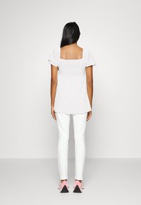 Blusa branca texturizada com mangas bufantes, decote quadrado, emparelhada com calças brancas e ténis cor-de-rosa com solas pretas.