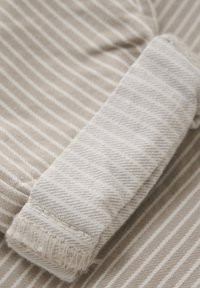 Ljust beige tyg med vertikala vita ränder; har en rullad manschett med fransade kanter, som visar ett texturerat vävmönster.