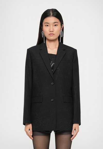 Blazer noir avec texture perforée, design à simple boutonnage, deux poches avant et fermeture à bouton. Stylé avec des collants transparents et un haut noir.