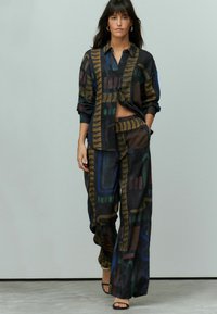 Completo a due pezzi composto da una camicia nera a maniche lunghe e pantaloni a gamba larga, entrambi con un vivace motivo geometrico astratto in varie sfumature.