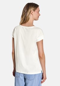 Hvid bomuld t-shirt med korte, rullede ærmer, rund halsudskæring, sideslids og en afslappet pasform, parret med blå denimbukser.
