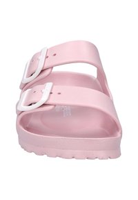 Roze slide sandaal van rubber met twee verstelbare witte gespsluitingen, een getextureerde voetbed en een dikke zool met een geribbeld patroon.