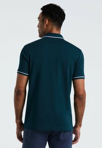 Polo shirt teal à manches courtes, avec un col et des bordures de manches blancs contrastants, texture unie et coupe droite. Vue de l'arrière.