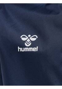 Marinblått tyg med en slät textur som har en vit Hummel-logotyp. Logotypen inkluderar en stiliserad biodlare och bladdesign.
