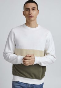 Sudadera de cuello redondo con tres bloques de color horizontales: blanco, beige y verde oliva. Tejido suave, puños y bajo acanalados. Diseño simple y moderno.