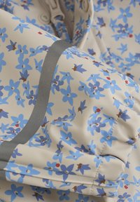 Blommönstrad tyg med ljusbeige bakgrund och blå blommor, accentuerad med grå kant och samlad ärmdetalj.