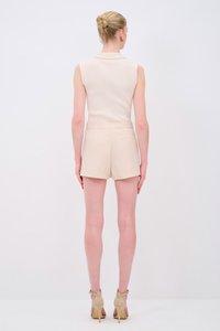 Top senza maniche beige aderente, in materiale a coste texturizzato; abbinato a pantaloni shorts beige a vita alta. Tessuto liscio, design minimalista.