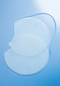 Gennemsigtige gel-patches med en glat overflade, der overlapper i en flydende form, sat mod en blød blå baggrund.
