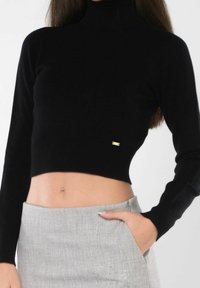Maglione corto nero a collo alto realizzato in materiale a coste, con maniche lunghe e un piccolo logo dorato dettagliato sull'orlo.