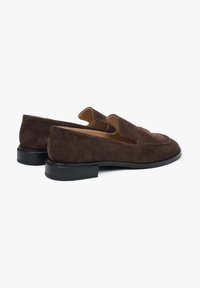 Brown suede loafers with a low heel, featuring curved openings on the sides, smooth interior, and a slightly pointed toe design.