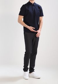 Chemise courte à manches en denim bleu marine avec un col boutonné, associée à un pantalon sombre et des baskets blanches. Design simple, texture lisse et coupe classique.