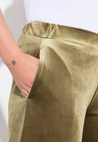 Olivgröna, blanka tygbyxor med resårmidja och sidoficka, som visar en jämn textur och en åtsittande passform.