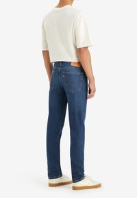 Blå denimjeans med en klassisk rak passform, med en läderlapp på baksidan, fem fickor och sömdekorationer. Bärs med en vit, kortärmad skjorta.