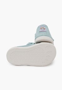 Zapatillas de lona azul claro con suela de goma blanca, que presentan un parche de un mono de dibujos animados en el talón y una suela de goma texturizada para mayor agarre.