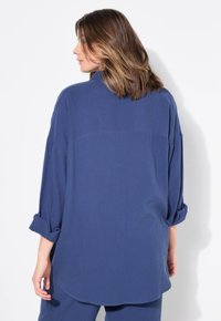 Camicia blu intrecciata con una vestibilità rilassata, spalle scese e maniche arrotolate. Tessuto testurizzato con un orlo leggermente curvo.