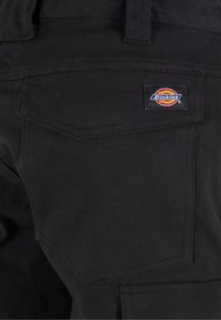 Pantaloni da lavoro neri in tessuto con molteplici tasche e un piccolo etichetta di marca sul retro. Il materiale sembra resistente e robusto.
