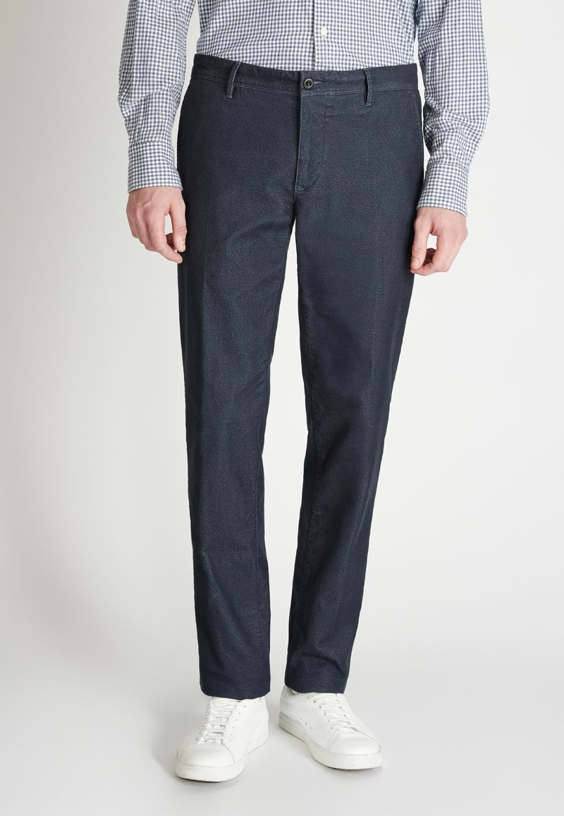 Pantalones texturizados en azul marino con un corte slim, con cierre frontal de botón, bolsillos laterales y combinados con zapatillas blancas.