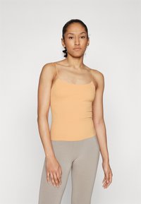 Heled oranž tank top õhukeste spaghetti rindadega, millele on lisatud heledat beeži legginsit; sile tekstuur ja minimalistlik disain.
