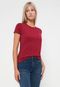 Bordo kratkosleeve majica s okruglim izrezom; mekana, glatka tekstura; s malim bijelim logotipom otisnutim na lijevoj strani prsnog područja.