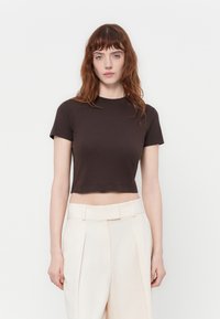 Hnedé skrátené tričko s krátkymi rukávmi, okr�úhlym výstrihom a mäkkou jersey textúrou, skombinované s nohavicami vysokého pásu v krémovej farbe.