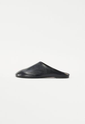 Mules negros de cuero sin talón con punta redondeada y suela plana baja. Textura suave con un diseño minimalista y sin herrajes visibles.