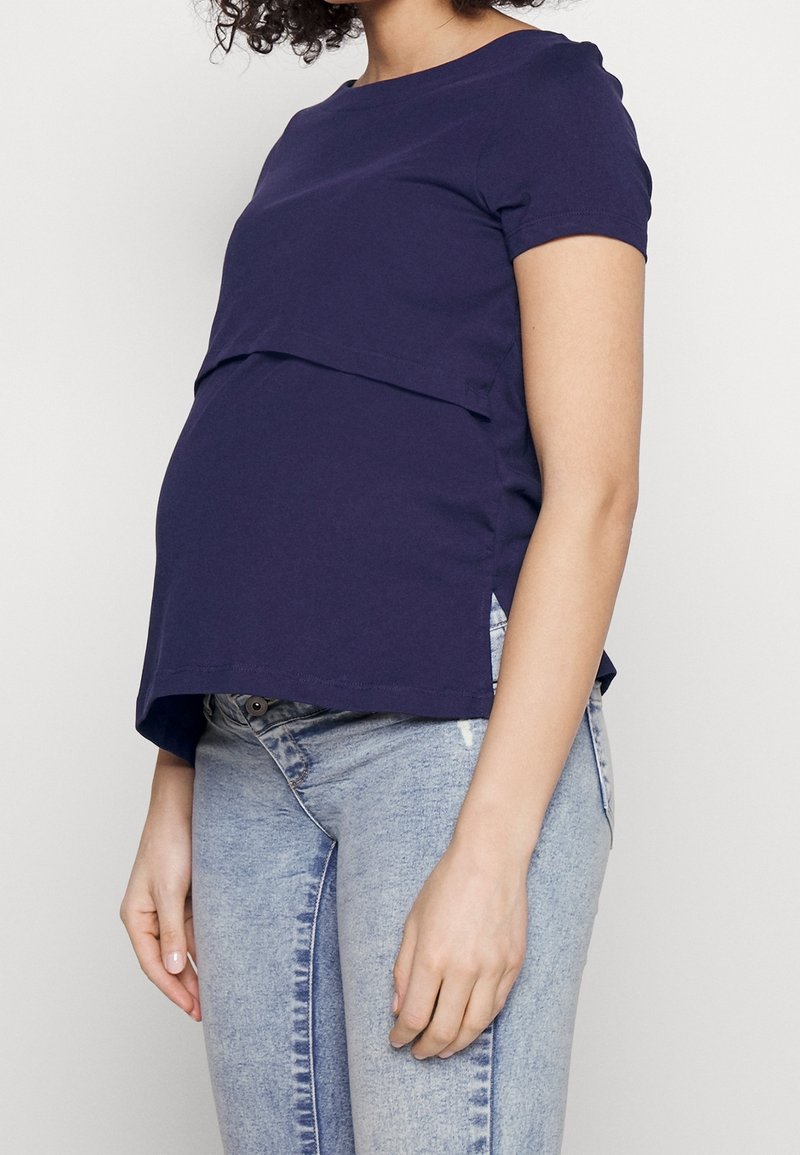 Navyblå amnings-T-shirt med korta ärmar, lagerdesign fram, rundad halsringning och sidokilar, kombinerad med ljusblå jeans.