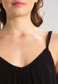 Mujer vistiendo una blusa sin mangas negra con borde de encaje, mostrando su cuello, clavícula y parte de su cara y cabello.