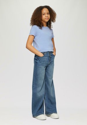 Helles, blaues T-Shirt mit kurzen Ärmeln kombiniert mit weit geschnittenen, hellblau gestreiften Jeans. Weiße Sneakers runden das Outfit ab.