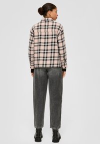 Karierte Flanellshirt in Pink, Schwarz und Weiß; lange Ärmel; Knopfverschluss; getragen mit hoch-taillierten, lockeren grauen Jeans und schwarzen Stiefeln.