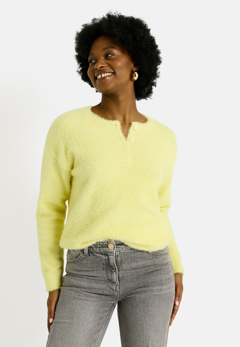 Pull en peluche jaune clair avec un col rond, fermeture à quatre boutons et manches longues, associé à un jean taille haute gris.