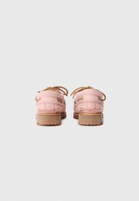 Pair of pink leather boat shoes with tan laces and thick brown rubber soles, viewed from the back on a white background.