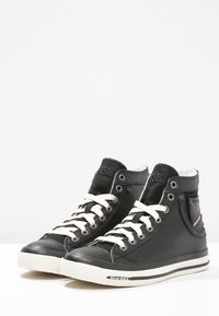 Czarne wysokie trampki wykonane ze skóry, z kremowymi sznurowadłami, wzmocnionym noskiem i boczną kieszenią z czerwonym akcentem.