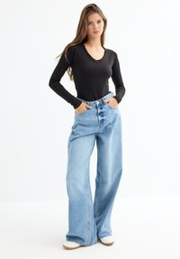 Top negro de manga larga combinado con jeans anchos de cintura alta en azul claro. Los jeans tienen un cierre frontal con botones y un diseño clásico de cinco bolsillos.