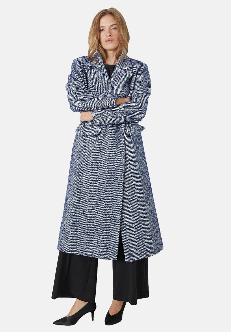 Cappotto lungo a motivo spina di pesce in blu navale e bianco, con colletto a scollo classico, vita con cintura e tasche laterali, realizzato in tessuto testurizzato.